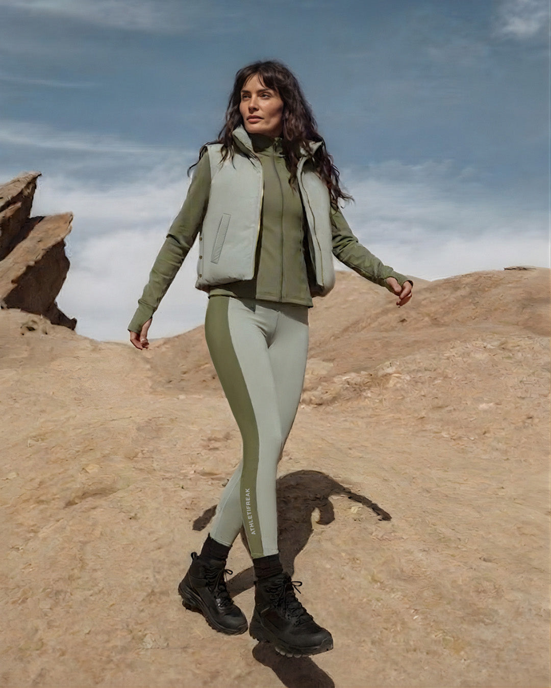 Woman in green jacket and leggings standing on a desert landscape
