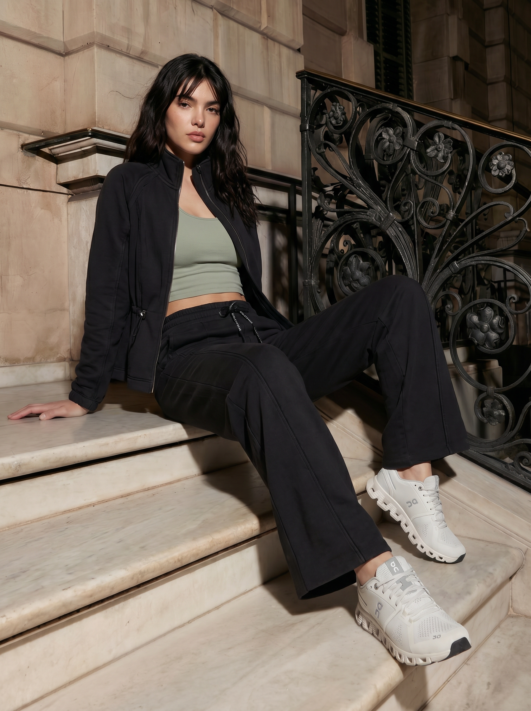Woman sitting on steps wearing a black jacket, green top, black pants, and white sneakers.