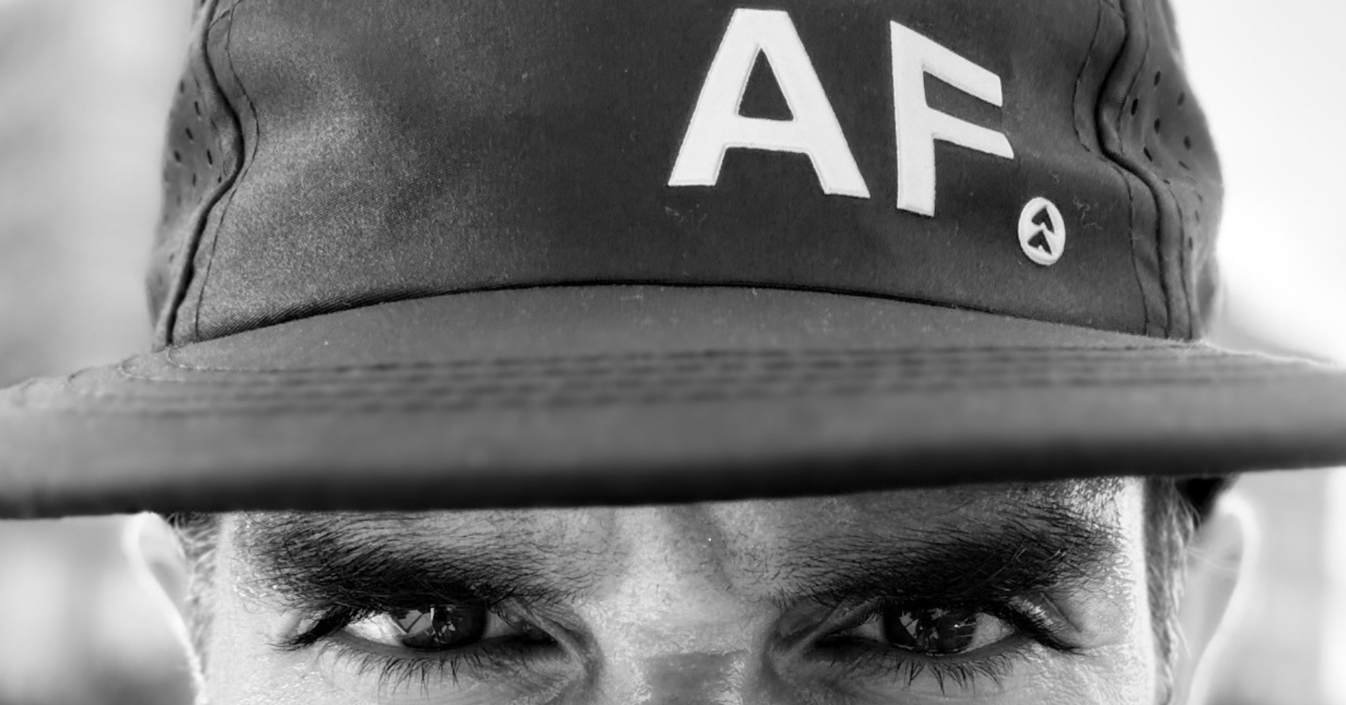 A close-up black and white photo of athlete wearing a dark running cap with large white letters 'AF' on the front.