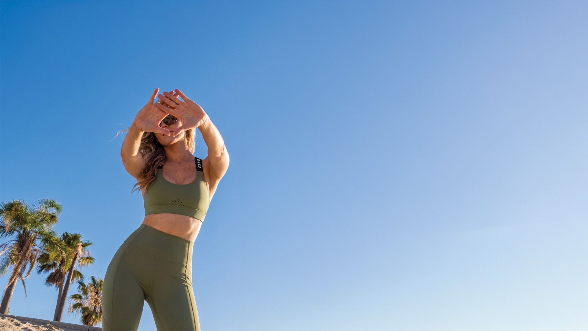 Woman in green athletic wear stretching outdoors with palm trees in the background