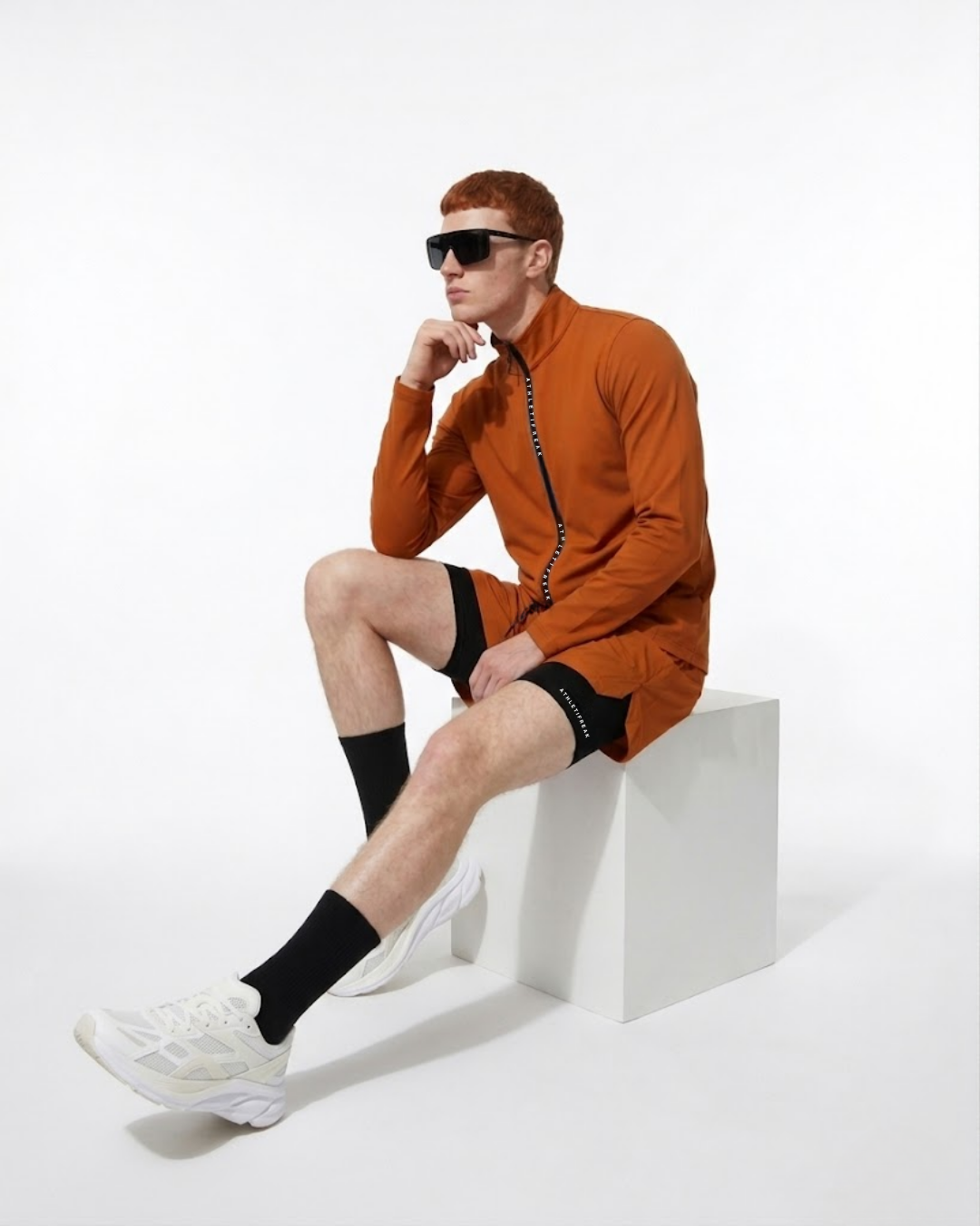 Person wearing an orange outfit with black socks and sunglasses on a white background