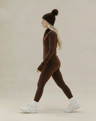 Person wearing a brown tracksuit and white sneakers on a beige background