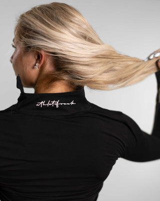 A women wearing black training half zip, showing Athletifreak's logo on collar